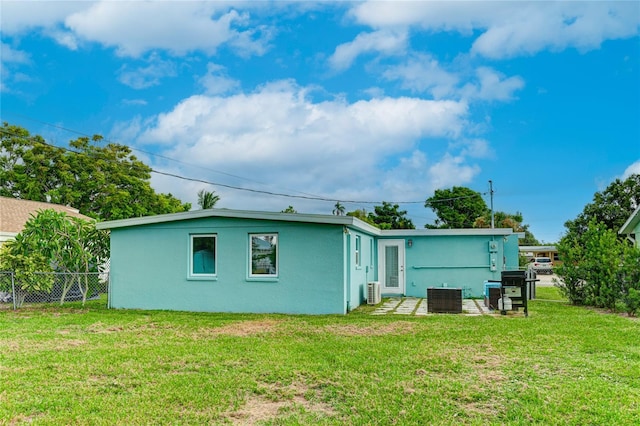 rear view of property with stucco siding, a yard, fence, and central air condition unit