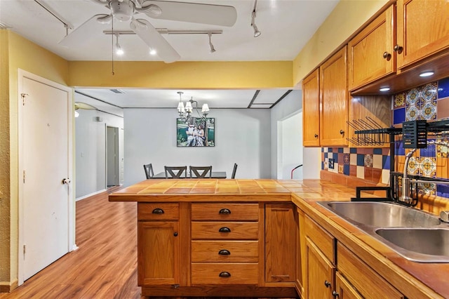 kitchen featuring ceiling fan with notable chandelier, light hardwood / wood-style flooring, kitchen peninsula, decorative backsplash, and track lighting