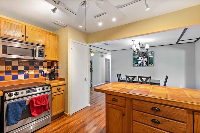 kitchen featuring tile countertops, rail lighting, wood-type flooring, decorative backsplash, and appliances with stainless steel finishes