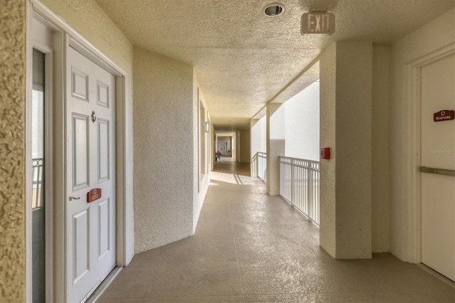 hall with plenty of natural light, a textured ceiling, and a textured wall