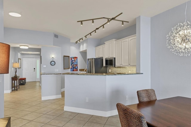 kitchen featuring appliances with stainless steel finishes, white cabinetry, a peninsula, and dark stone countertops