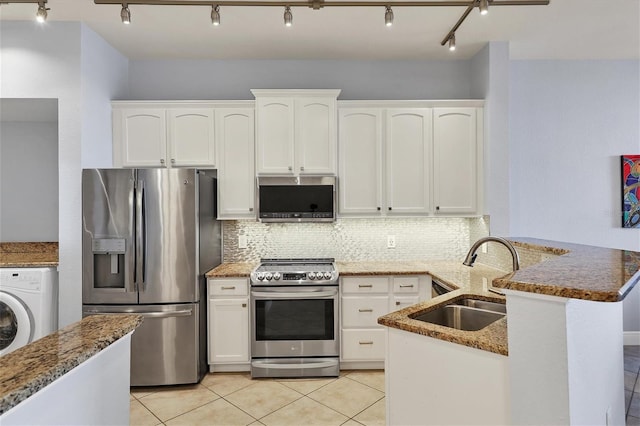 kitchen with appliances with stainless steel finishes, white cabinets, a sink, washer / dryer, and a peninsula