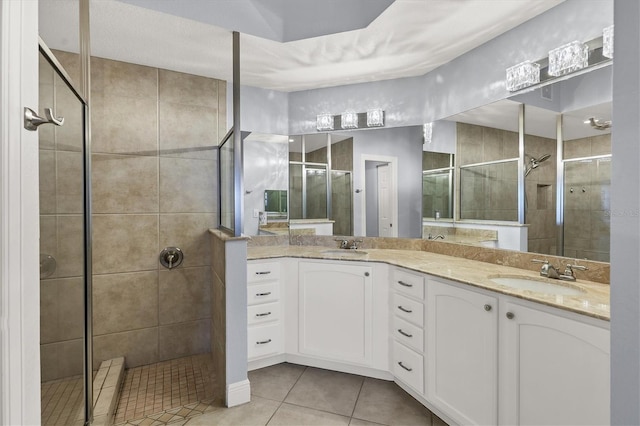 bathroom featuring tile patterned flooring, tiled shower, a sink, and double vanity