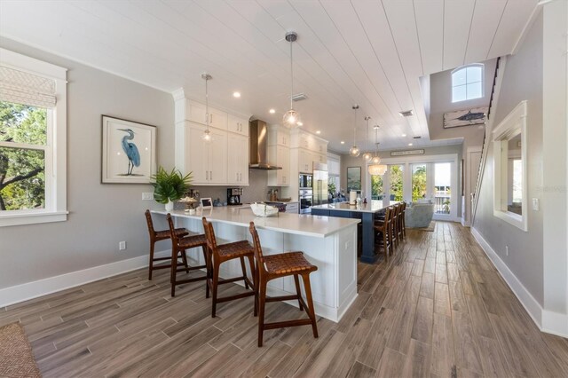 kitchen featuring wood-type flooring, wall chimney exhaust hood, a breakfast bar area, kitchen peninsula, and white cabinets