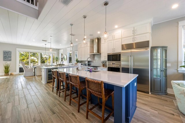 kitchen featuring a breakfast bar, a spacious island, decorative light fixtures, wall chimney exhaust hood, and built in appliances