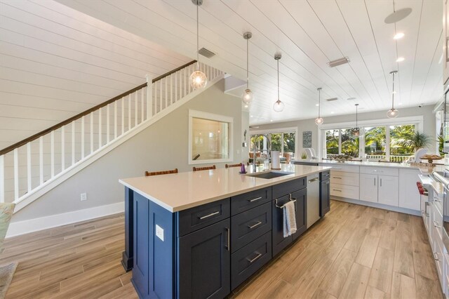 kitchen featuring a kitchen island with sink, white cabinets, light wood-type flooring, and hanging light fixtures