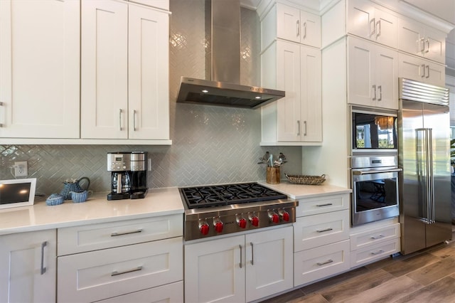 kitchen featuring dark hardwood / wood-style flooring, wall chimney exhaust hood, tasteful backsplash, white cabinetry, and built in appliances