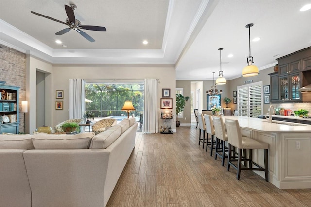 living room with crown molding, dark hardwood / wood-style flooring, sink, a tray ceiling, and ceiling fan