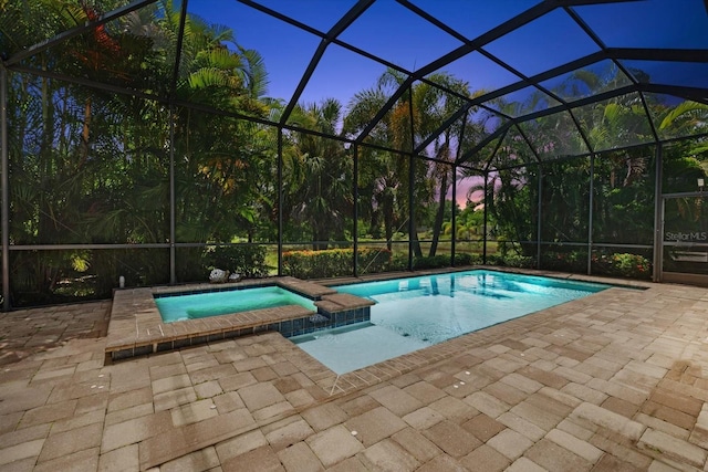 pool at dusk with a patio, a lanai, and an in ground hot tub