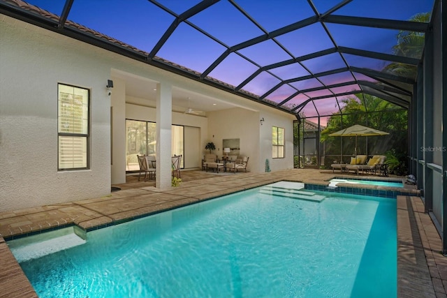 pool at dusk with glass enclosure, a patio, ceiling fan, and an in ground hot tub