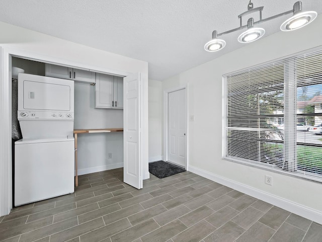 interior space featuring laundry area, baseboards, a textured ceiling, and stacked washing maching and dryer