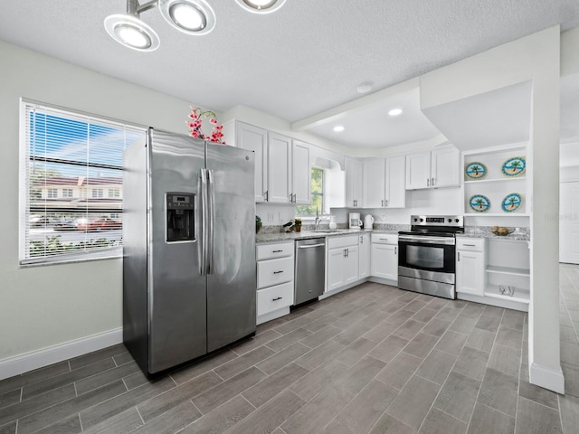 kitchen featuring a sink, white cabinets, appliances with stainless steel finishes, light stone countertops, and open shelves