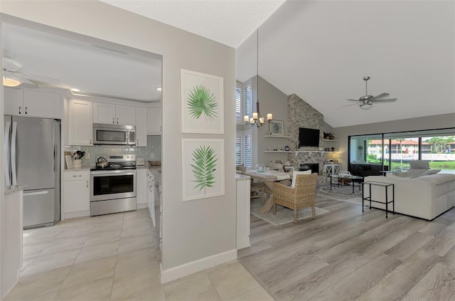 kitchen with a stone fireplace, stainless steel appliances, ceiling fan with notable chandelier, and white cabinetry