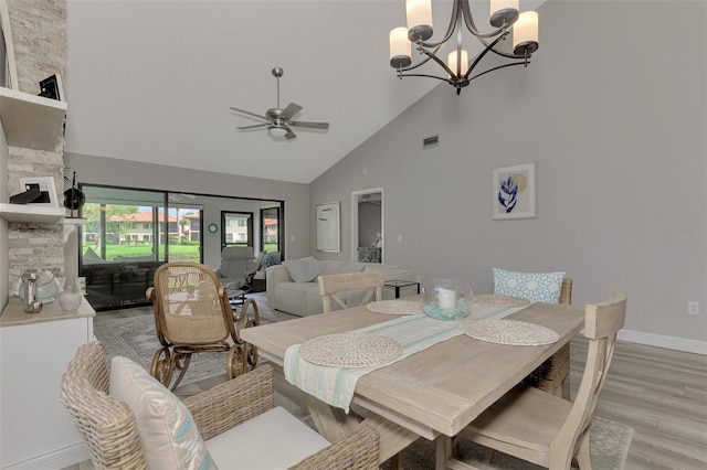 dining room featuring high vaulted ceiling, ceiling fan with notable chandelier, a fireplace, and light hardwood / wood-style flooring