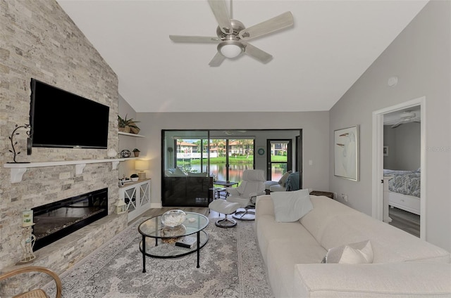 living room featuring high vaulted ceiling, ceiling fan, light hardwood / wood-style floors, and a stone fireplace