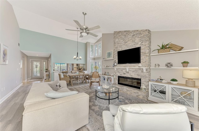 living room with light hardwood / wood-style flooring, ceiling fan with notable chandelier, a stone fireplace, high vaulted ceiling, and a textured ceiling