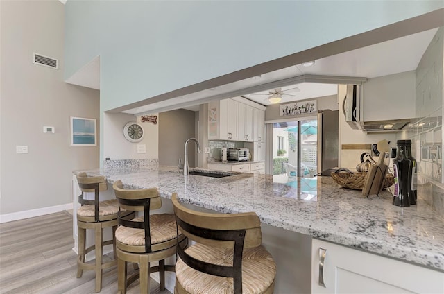 kitchen featuring white cabinets, light wood-type flooring, sink, ceiling fan, and a breakfast bar