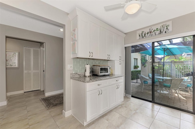 kitchen featuring white cabinetry, backsplash, light tile patterned floors, light stone countertops, and ceiling fan