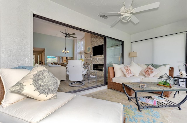 living room with a large fireplace, ceiling fan with notable chandelier, and light tile patterned floors