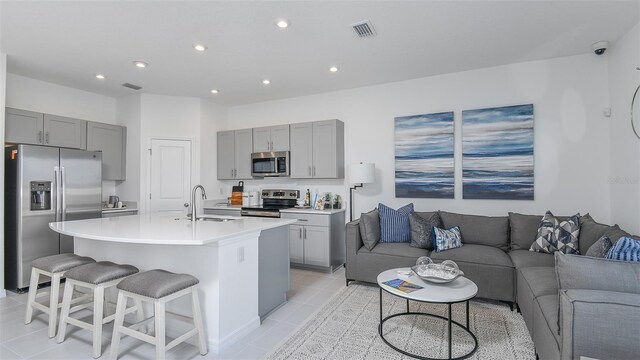 kitchen featuring gray cabinets, an island with sink, appliances with stainless steel finishes, light tile patterned floors, and sink