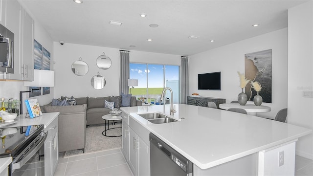 kitchen with light countertops, open floor plan, a kitchen island with sink, a sink, and dishwashing machine