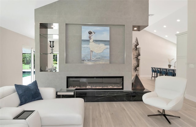 living area featuring recessed lighting, wood finished floors, a high ceiling, and a glass covered fireplace