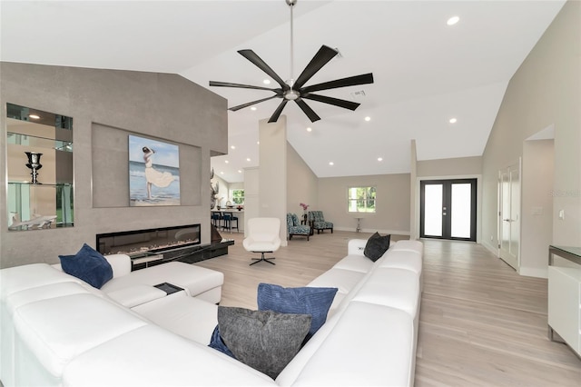 living room featuring french doors, high vaulted ceiling, light wood-style flooring, and a fireplace