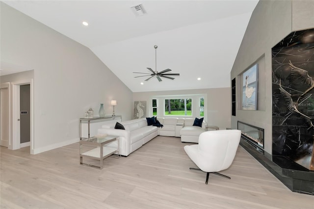 living area featuring a high end fireplace, visible vents, light wood-type flooring, and vaulted ceiling