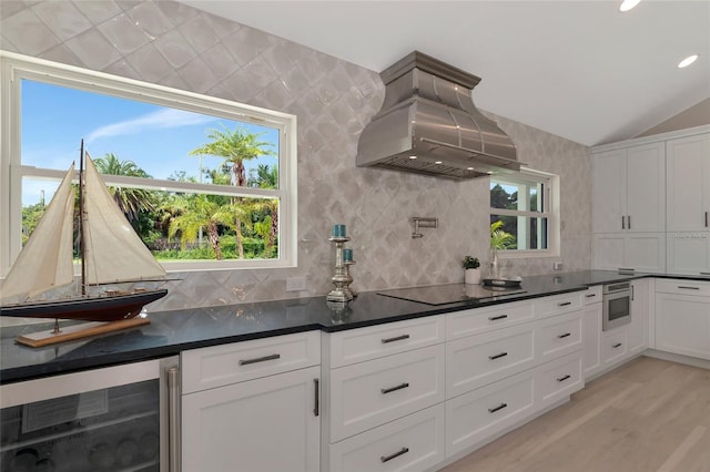 kitchen featuring island exhaust hood, black electric stovetop, dark countertops, and beverage cooler