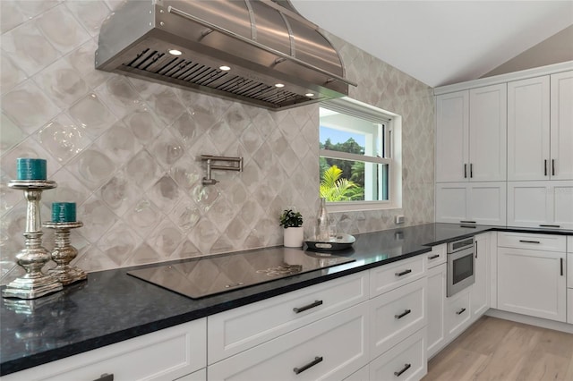 kitchen with black electric stovetop, dark countertops, exhaust hood, and white cabinetry