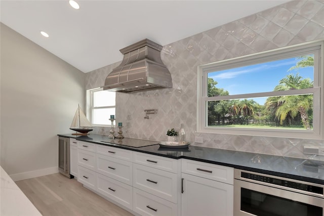 kitchen featuring black electric stovetop, decorative backsplash, light wood-style flooring, exhaust hood, and white cabinetry