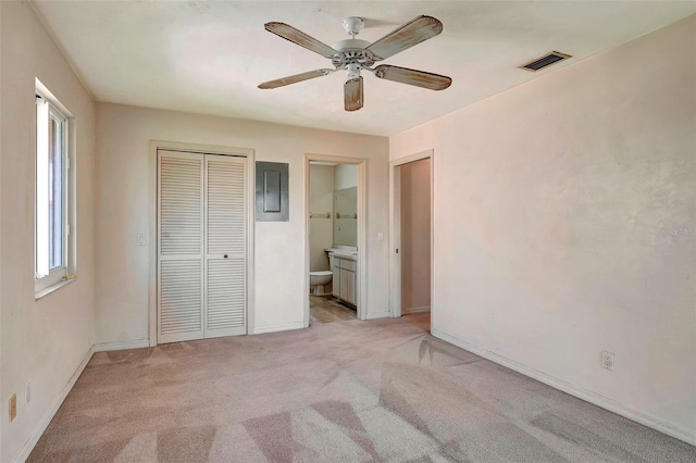 unfurnished bedroom with light carpet, ceiling fan, connected bathroom, electric panel, and a closet