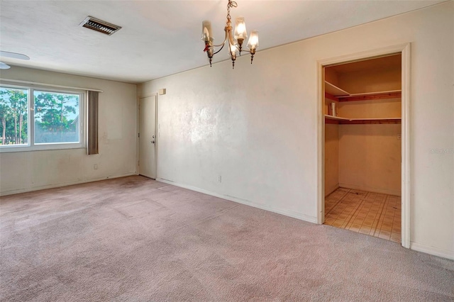 unfurnished bedroom with a closet, light colored carpet, a walk in closet, and an inviting chandelier