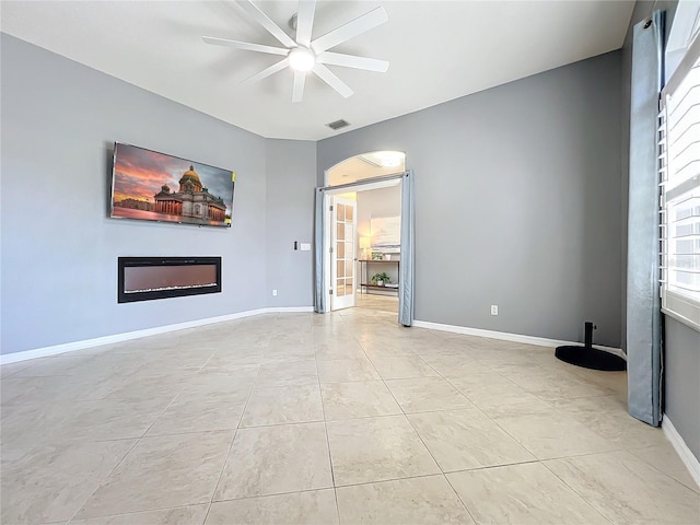 unfurnished room featuring ceiling fan, light tile patterned floors, visible vents, baseboards, and a glass covered fireplace