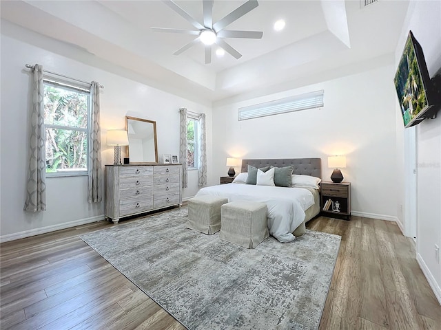 bedroom with multiple windows, a tray ceiling, and wood finished floors