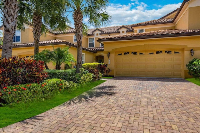 mediterranean / spanish home with decorative driveway, an attached garage, a tile roof, and stucco siding