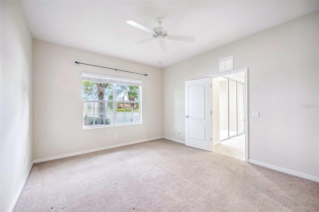 empty room featuring a ceiling fan, light colored carpet, and baseboards