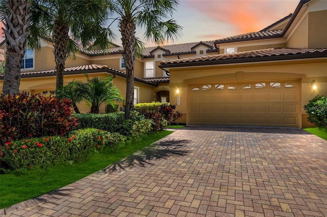 mediterranean / spanish house featuring decorative driveway, a tile roof, an attached garage, and stucco siding