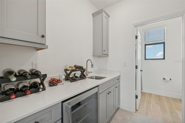 kitchen with beverage cooler, gray cabinets, sink, and light wood-type flooring