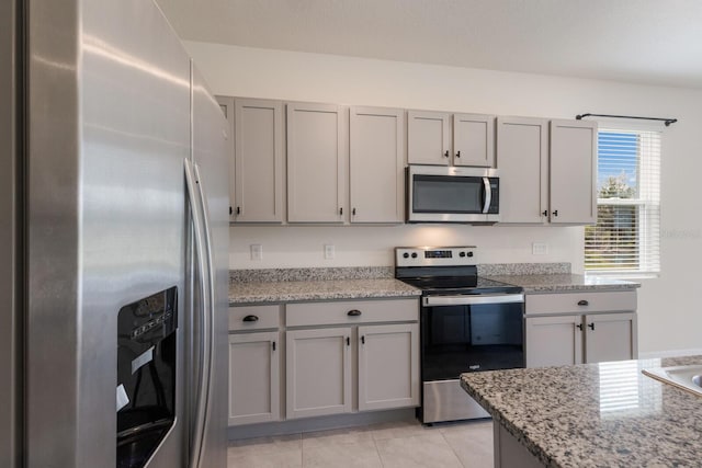 kitchen featuring light tile patterned floors, appliances with stainless steel finishes, light stone counters, and gray cabinetry