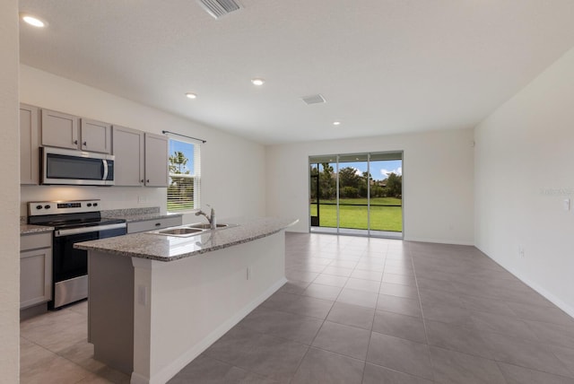 kitchen with sink, a kitchen island with sink, light tile patterned floors, stove, and gray cabinets