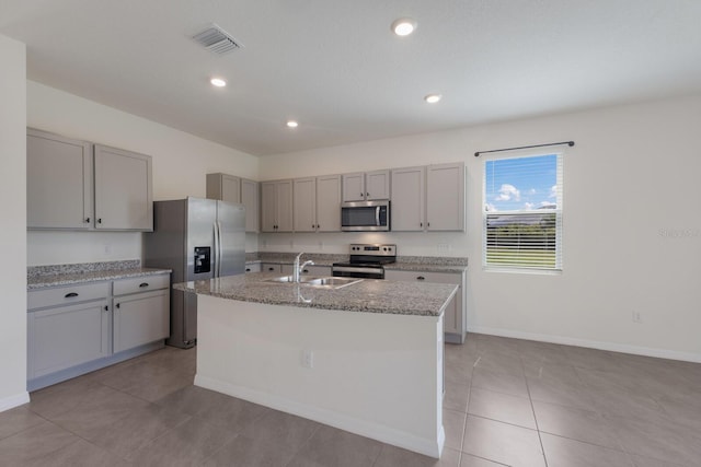 kitchen with gray cabinets, a kitchen island with sink, light stone countertops, light tile patterned floors, and stove