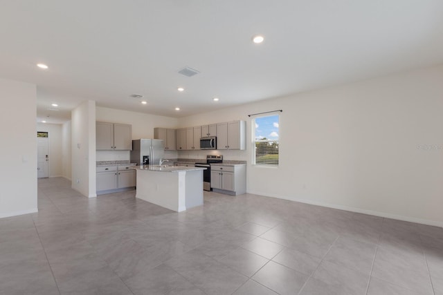 kitchen featuring gray cabinetry, stainless steel appliances, an island with sink, and light tile patterned floors