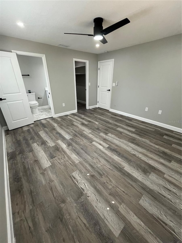 unfurnished bedroom featuring a walk in closet, ensuite bath, a closet, ceiling fan, and dark hardwood / wood-style floors