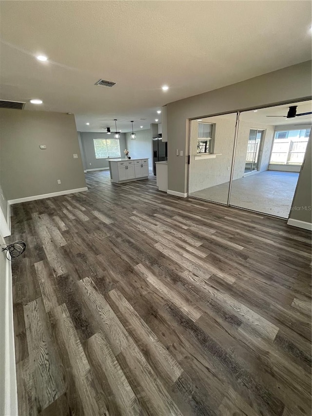 unfurnished living room featuring dark wood-type flooring and ceiling fan