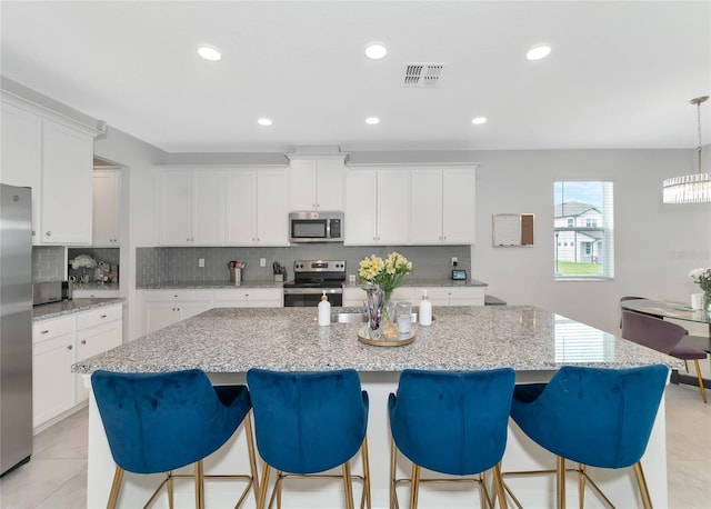 kitchen with tasteful backsplash, white cabinets, light tile patterned floors, a center island, and stainless steel appliances