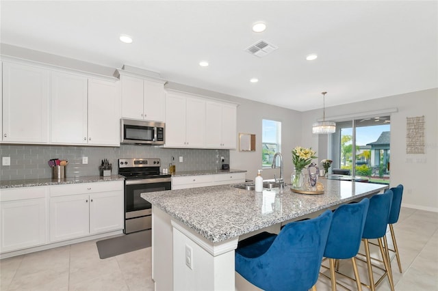 kitchen with a kitchen island with sink, stainless steel appliances, visible vents, white cabinets, and a sink