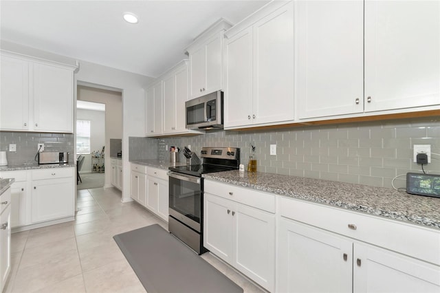 kitchen with light tile patterned floors, appliances with stainless steel finishes, light stone counters, and backsplash