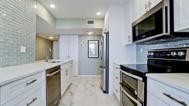 kitchen with backsplash, white cabinets, appliances with stainless steel finishes, light stone countertops, and sink