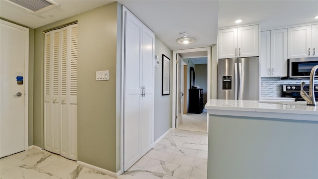 kitchen featuring white cabinets, tasteful backsplash, light tile patterned flooring, and stainless steel appliances